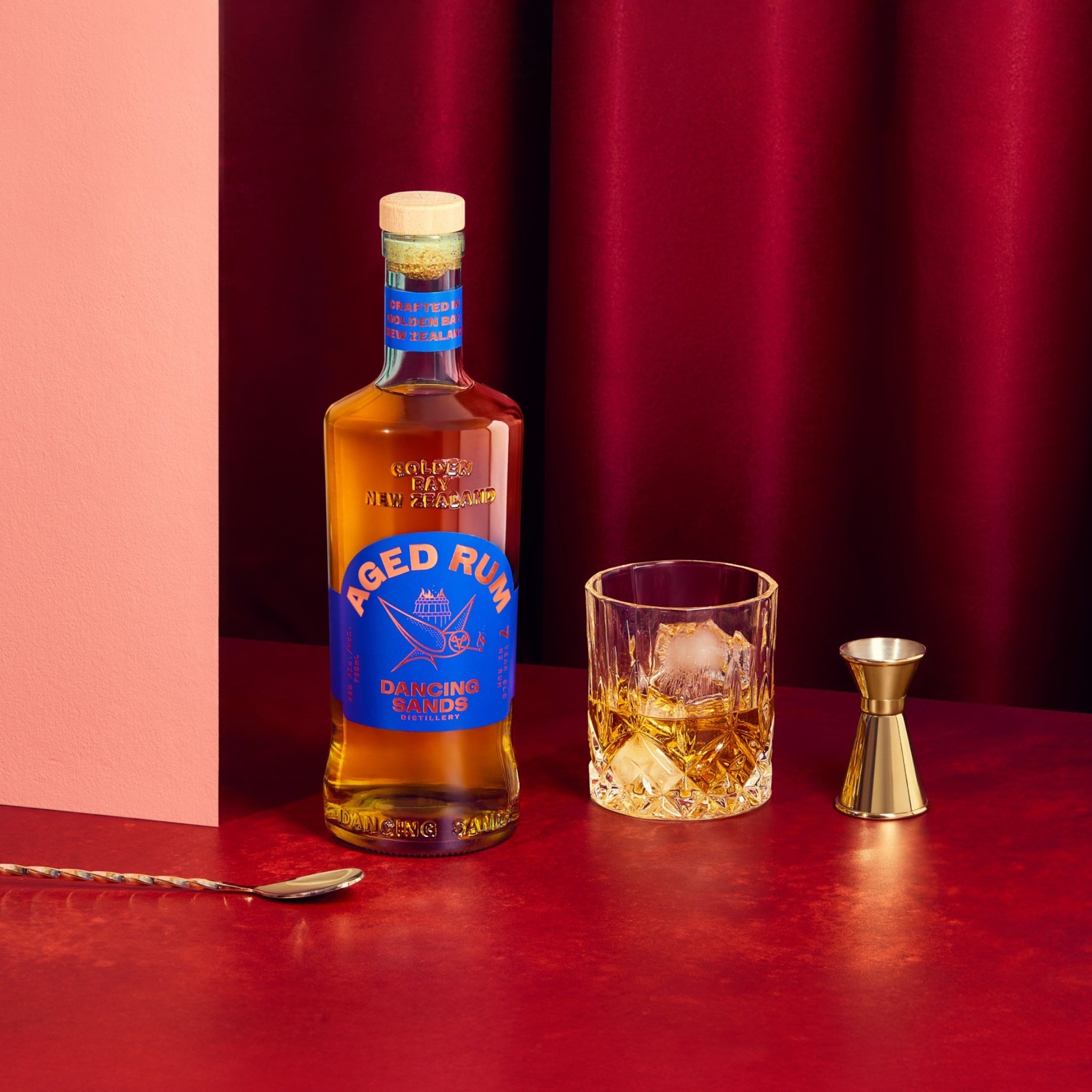 Bottle of Aged Rum with a glass of cocktail and jigger on a red surface
