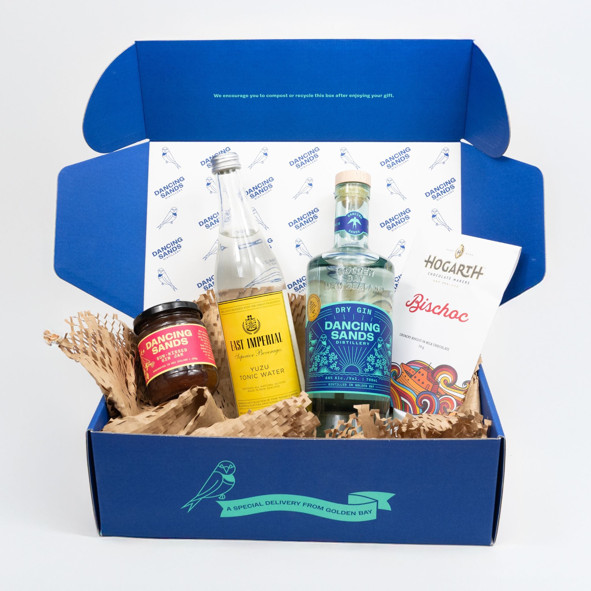 Open blue gift box with Dry Gin, Yuzu Tonic bottle, Hogarth "bischoc' Chocolate and Gin Jam on a white background