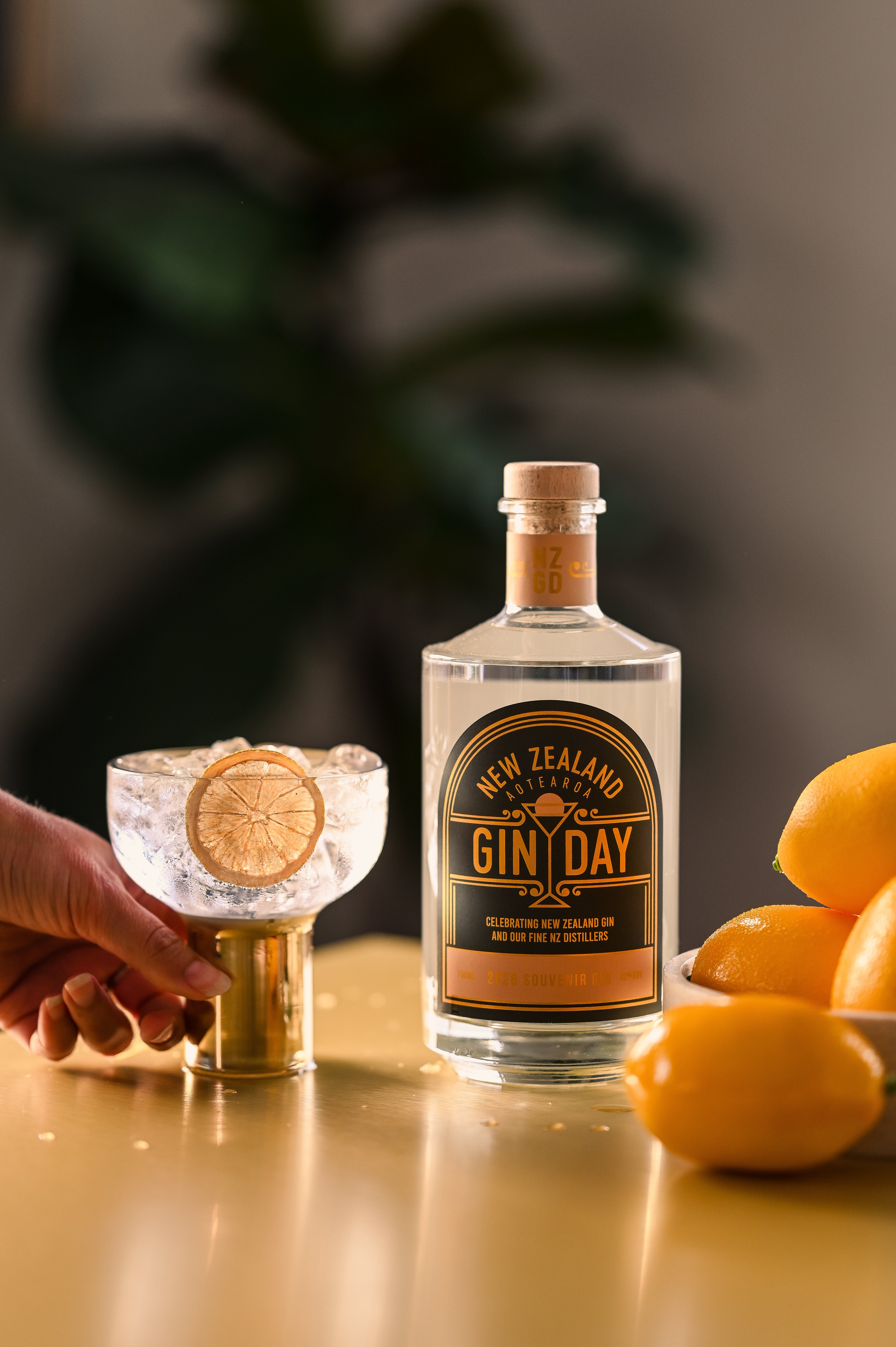 Bottle of NZ Gin Day next to a bowl of lemons with a hand on a cocktail glass next to it