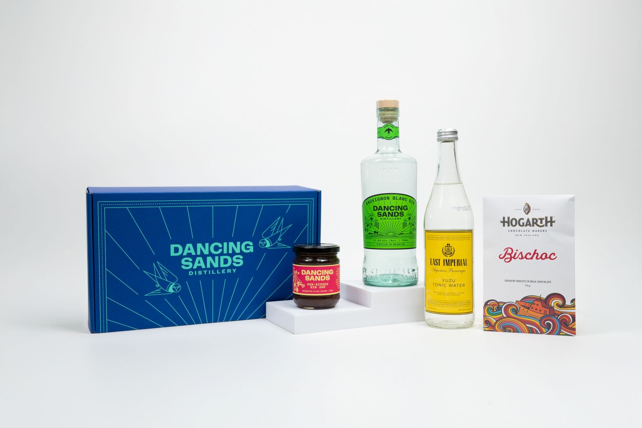 Collection of a Sauvignon Blanc Gin bottle, Tonic, Gin Jam and Hogarth 'Bischoc' Chocolate with a 'Dancing Sands' Box on a white background