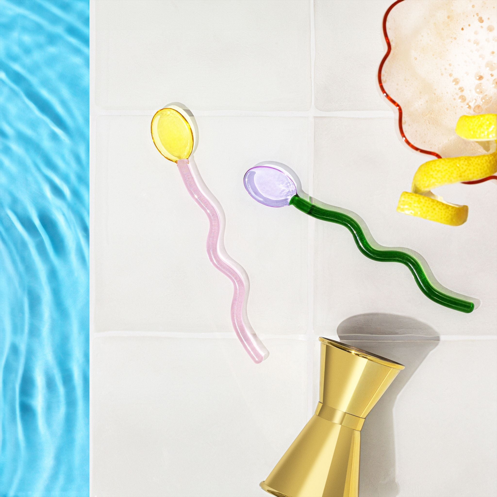 Colorful glass straws with a gold jigger on a white background