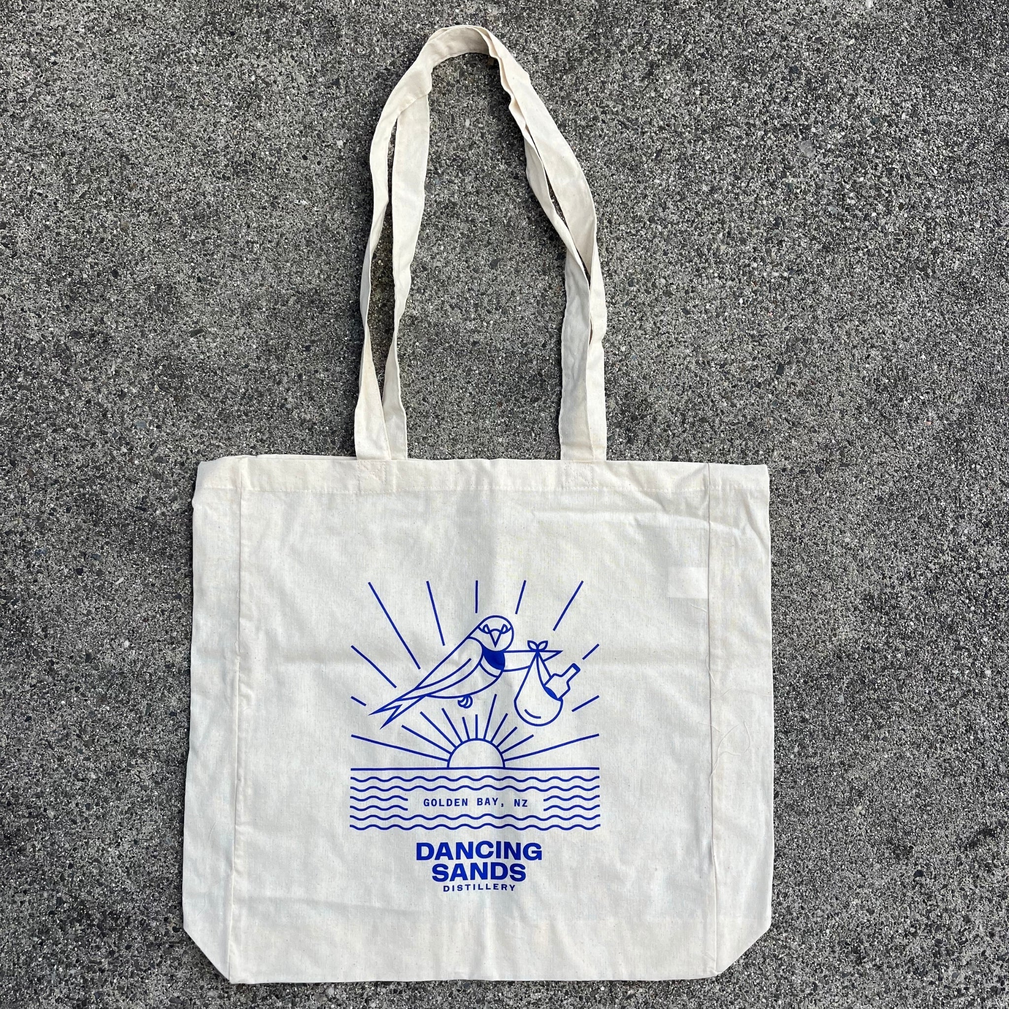 White Dancing Sands tote bag with blue graphic design on a gray surface