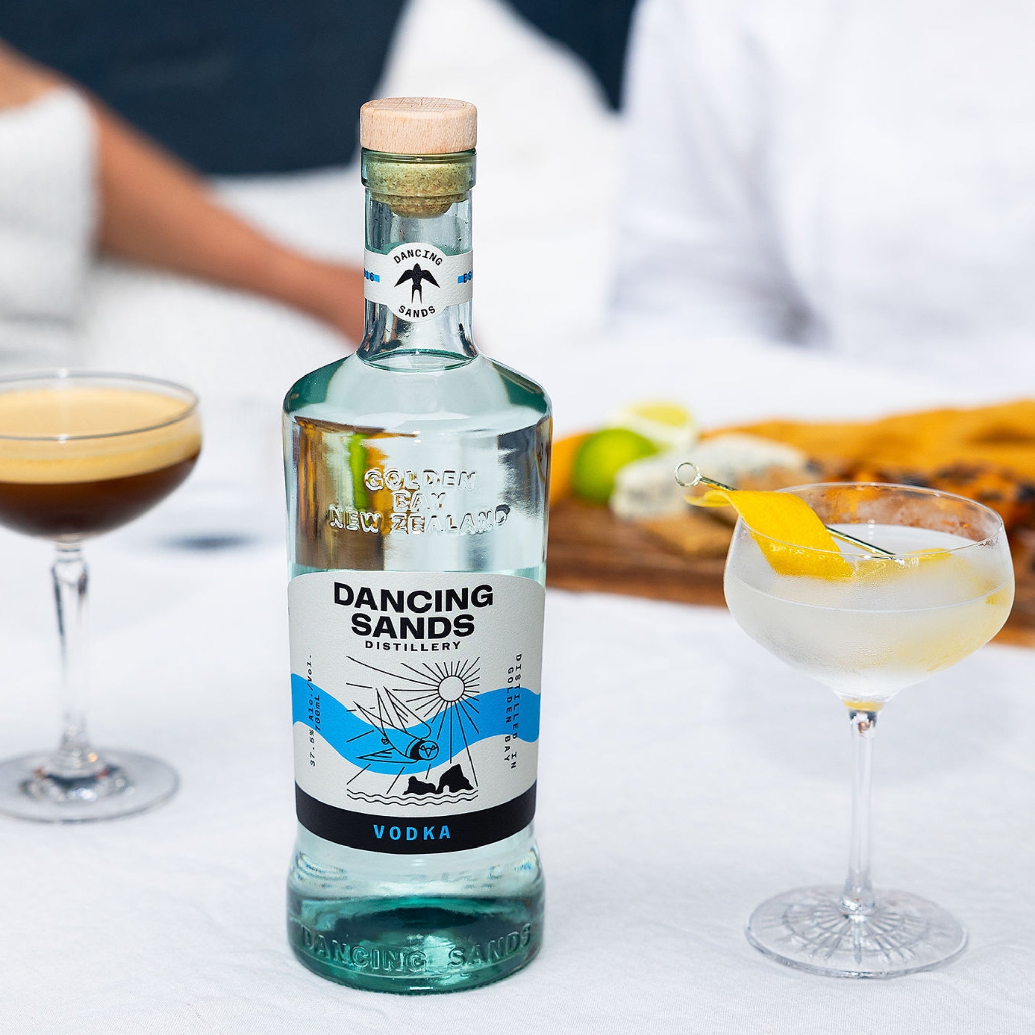 Bottle of Dancing Sands Vodka with cocktails in the background