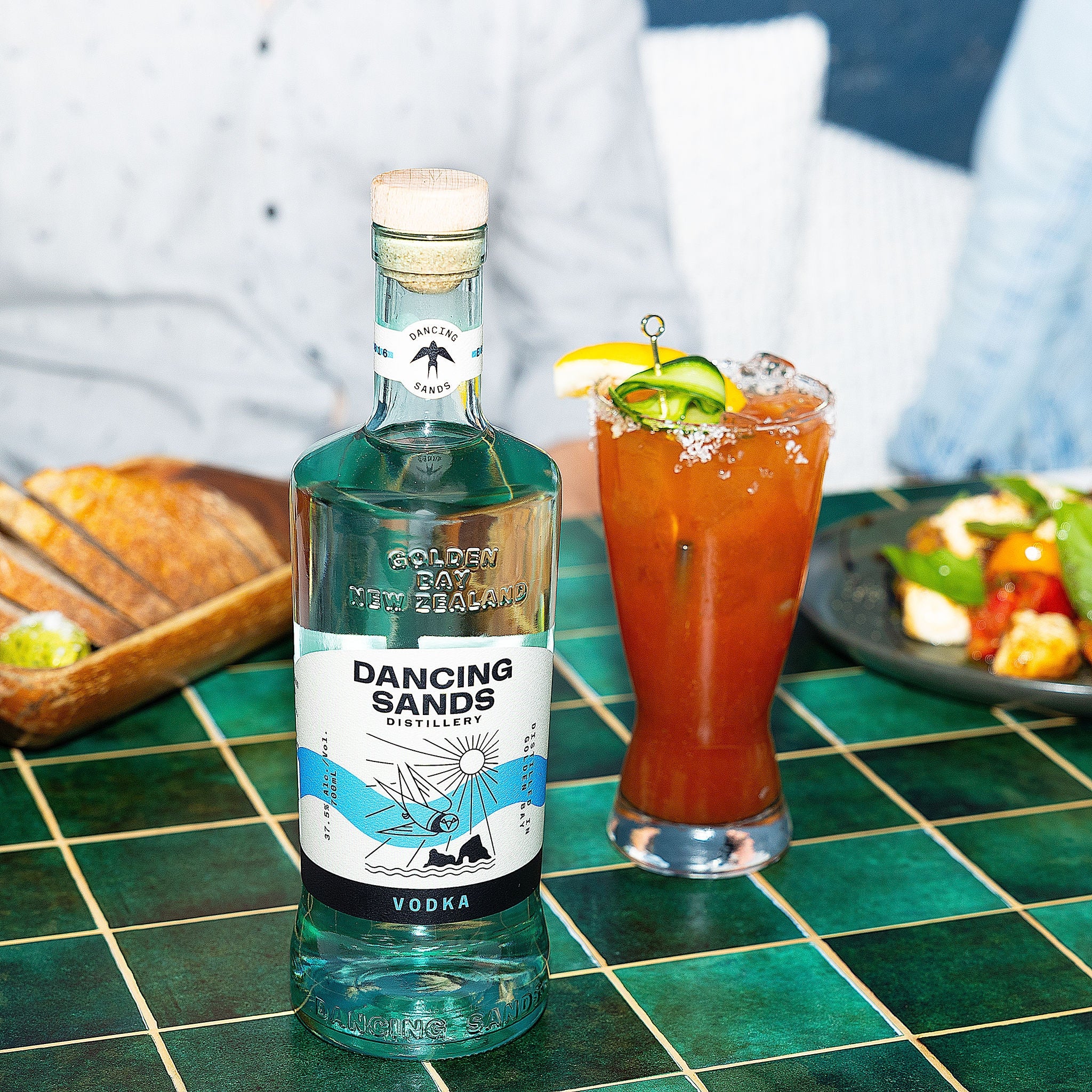 Bottle of Dancing Sands vodka on a table with a bloody mary cocktail in the background