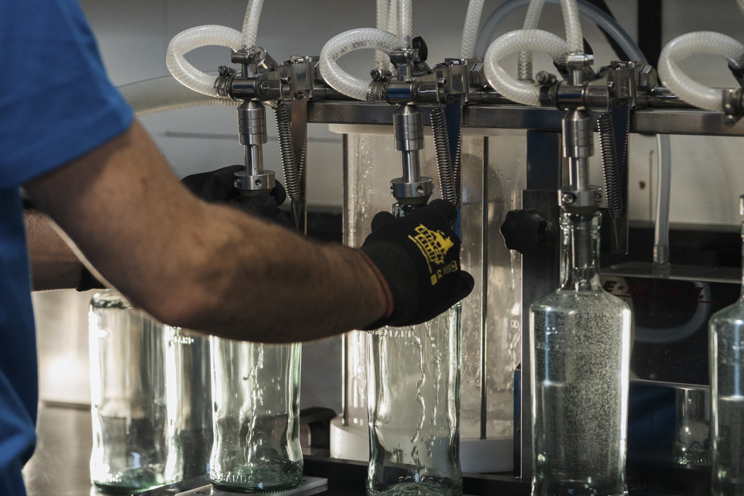 Person operating a bottling machine with clear bottles on an assembly line.