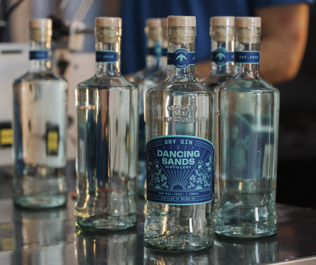 Bottles of Dancing Sands Dry Gin on a reflective surface with a blurred background